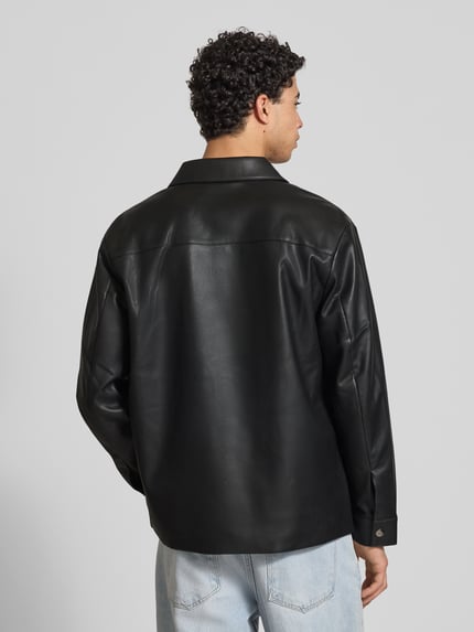 Męski model nosi Regular Fit Hemdjacke in Leder-Optik von Calvin Klein Jeans, czarny kolor, wykładany kołnierz, kieszenie na piersi, listwa guzikowa, sportowe mankiety, długość tyłu w rozmiarze M: 73 cm, szerokość ramion w rozmiarze M: 50 cm, długość rękawów w rozmiarze M: 65 cm, imitacja skóry, gładka tekstura, widok całej sylwetki z tyłu.