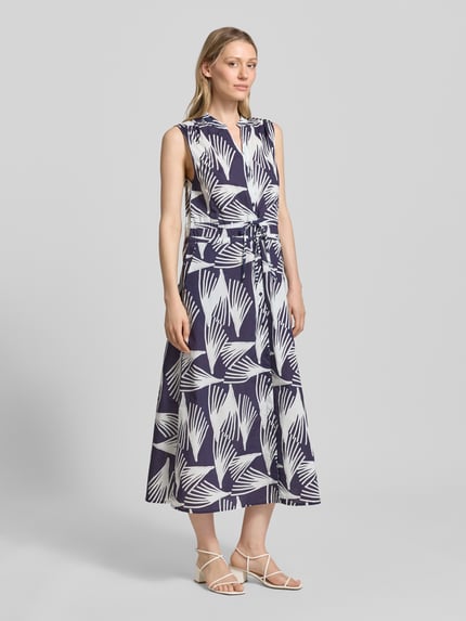 Frauenmodel trägt Hemdblusenkleid mit V-Ausschnitt und Bindegürtel Modell 'Lani' von GUIDO MARIA KRETSCHMER WOMAN, Reine Baumwolle, A-Linie, Allover-Look, Midikleid, Knopfleiste, dunkle und helle Farben, fließende Textur, Ganzkörperansicht von vorne.