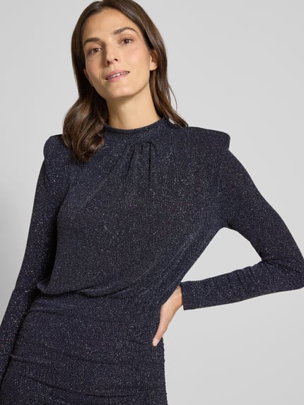 Vrouwenmodel draagt knielang kleed met schoudervullingen van Rich & Royal, glanzende stof, getailleerd, detailopname bovenlichaam.
