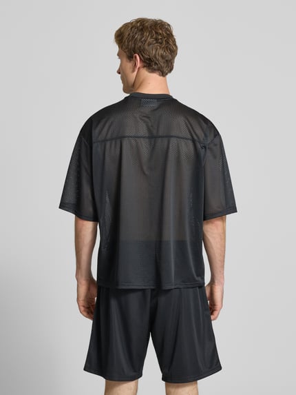 Männermodel trägt T-Shirt aus Mesh mit Logo-Print von REVIEW, schwarzes Mesh, Loose-Fit, Rundhalsausschnitt, Rückenlänge 66 cm, Ganzkörperansicht Rückansicht.