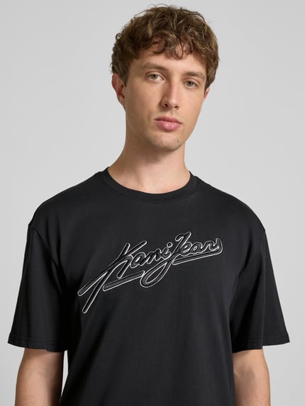 Männermodel trägt Oversized Fit T-Shirt mit Logo-Stitching von KARL KANI, schwarze Farbe, Reine Baumwolle, Rundhalsausschnitt, Nahaufnahme Oberkörper, Rückenlänge bei Größe M: 72 cm.