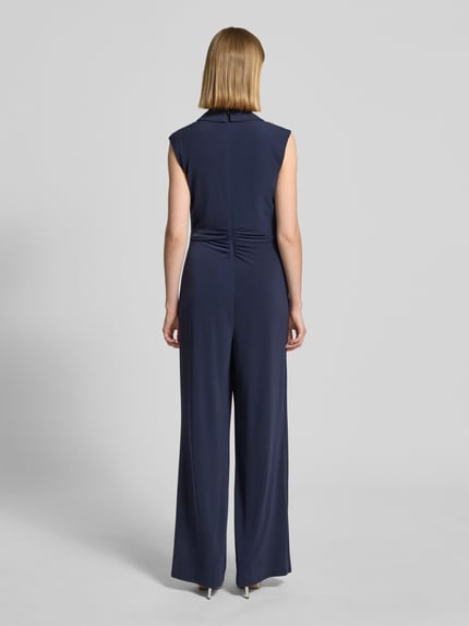 Frauenmodel trägt Jumpsuit in Wickel-Optik mit Schalkragen von Vera Mont in Dunkelblau, Material-Mix mit Stretch-Anteil, Taillierter Schnitt, Raffungen, Rückseitiger Reißverschluss, Rückenlänge 41 cm, Brustweite 45 cm, Ärmellänge 14 cm, Gesamtlänge 154 cm, Innenbeinlänge 86 cm, fließende Textur, Ganzkörperansicht Rückansicht.
