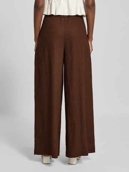 Frauenmodel trägt Wide Fit Leinen-Hose aus Leinen-Mix von Rich & Royal in Braun, elastischer Bund, Bundfalten, Ganzkörperansicht Rückansicht.