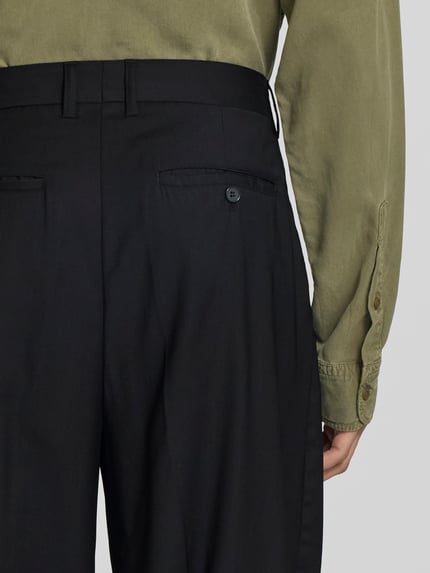 Männermodel trägt Wide Fit Stoffhose aus Woll-Mix von Filippa K, Schwarz mit Gesäßtaschen, Knopf-Reißverschluss, Detailaufnahme Rückansicht.