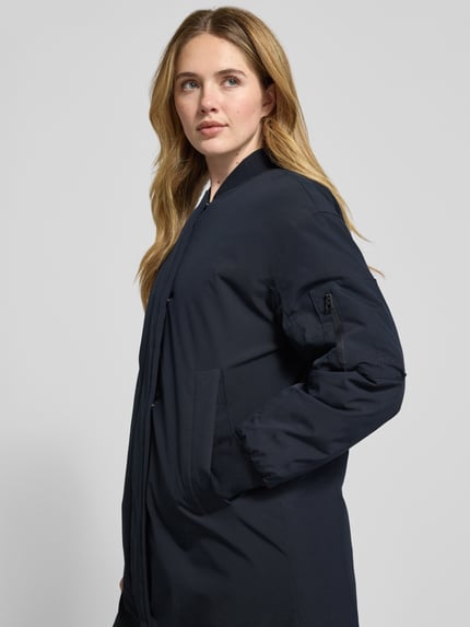 Frauenmodel trägt Regular Fit Parka mit College-Kragen von Marc O'Polo, Optik: Unifarben, Passform: Regular-Fit, Kragenform: College-Kragen, Verschluss: verdeckter Zweiwege-Reißverschluss, Druckknopfleiste, Applikation: Label-Stitching, Ärmelform: Langarm, Ärmelabschluss: gerippt, Taschen: seitliche Eingrifftaschen, Ärmeltasche mit Reißverschluss, Materialverarbeitung: feine Webstruktur, dunkle Farbe, glatte Textur, Nahaufnahme Oberkörper.