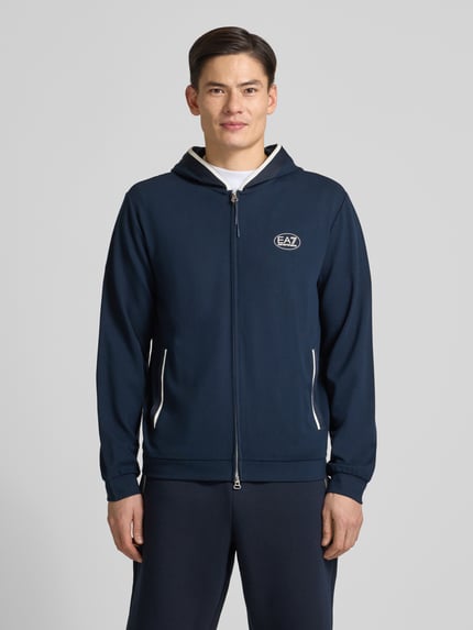 Männermodel trägt Sweatjacke mit Logo und Zweiwege-Reißverschluss von EA7 Armani, Viskose-Mix, Regular Fit, Kapuze, Eingrifftaschen, Ganzkörperansicht von vorne.