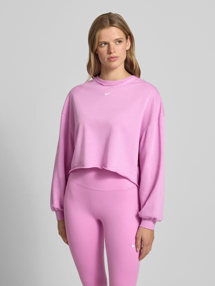Frauenmodel trägt Cropped Sweatshirt mit Logo-Stitching von Nike in Rosa mit Rundhalsausschnitt, Relaxed Fit, Ganzkörperansicht von vorne.