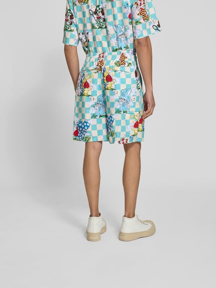 Männermodel trägt Shorts mit Allover-Motiv-Print von Kenzo, bawełna, krój relaxed fit, pas elastyczny, zapięcie na guzik i zamek błyskawiczny, długość wewnętrzna nogawki w rozmiarze M: 41 cm, szerokość w rozmiarze M: 18 cm, kolorowe kwadraty i motywy, tekstura gładka, Ganzkörperansicht Rückansicht.
