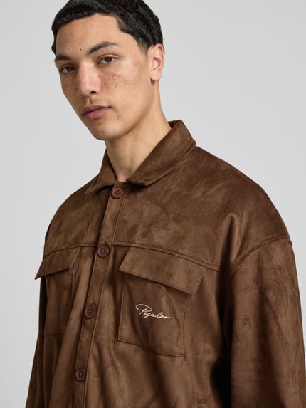 Männermodel trägt Relaxed Fit Hemdjacke mit Brusttaschen Modell 'Madikeri' von Pegador in brauner Leder-Optik, Nahaufnahme Oberkörper.
