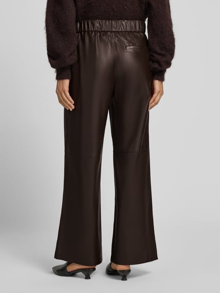 Frauenmodel trägt Wide Fit Hose in Leder-Optik von COMMA, dunkelbraune Farbe, elastischer Bund, Eingrifftaschen, Ganzkörperansicht Rückansicht.