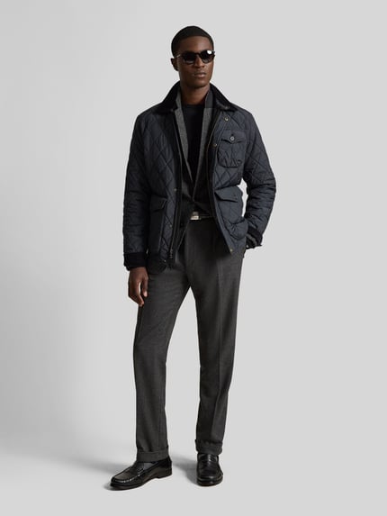 Męski model nosi Regular Fit Steppjacke mit Druckknopfleiste von Polo Ralph Lauren, jednokolorowy, wykładany kołnierz, długi rękaw, listwa z zatrzaskami, wyhaftowane logo, kieszenie z patką i kieszeń wewnętrzna, wykończenie: stepp-webware, pełen widok z przodu.