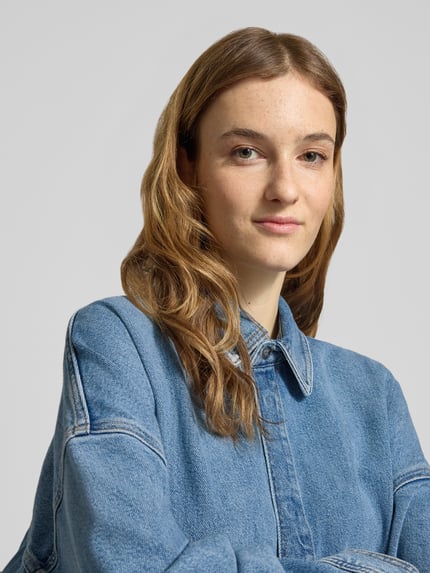 Frauenmodel trägt Jeansbluse mit Hemdblusenkragen von Calvin Klein Jeans aus reiner Baumwolle in Denim-Optik, Nahaufnahme Oberkörper.