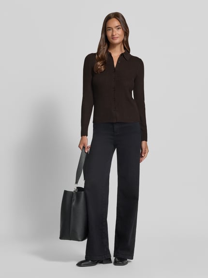 Frauenmodel trägt Cardigan aus Lanawolle mit Polokragen Modell 'ARHANYA' von DRYKORN, schwarz, Ripp-Optik, Slim Fit, Ganzkörperansicht von vorne.