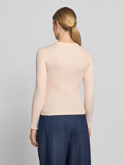Frauenmodel trägt Slim Fit Langarmshirt aus reiner Baumwolle von Lacoste in Hellrosa, glatte Struktur, kombiniert mit blauer Hose, Ganzkörperansicht Rückansicht. Damen T-Shirt von Lacoste.