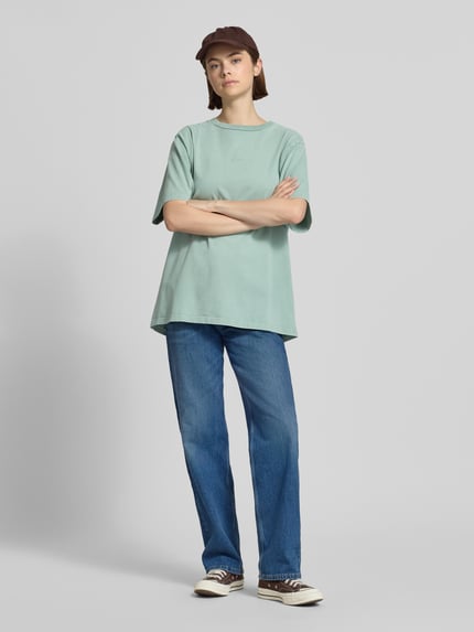 Frauenmodel trägt Oversized T-Shirt mit Label-Stitching von OH APRIL aus reiner Baumwolle, Rundhalsausschnitt, Ganzkörperansicht von vorne.
