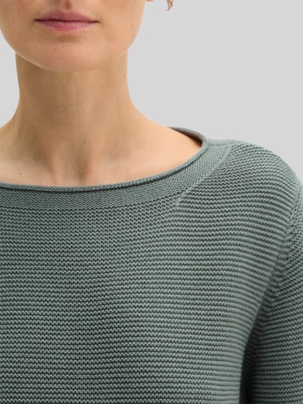 Frauenmodel trägt Regular Fit Pullover aus reiner Baumwolle von MARC O’POLO in unifarbener Strickoptik mit U-Boot-Ausschnitt, Nahaufnahme Oberkörper.