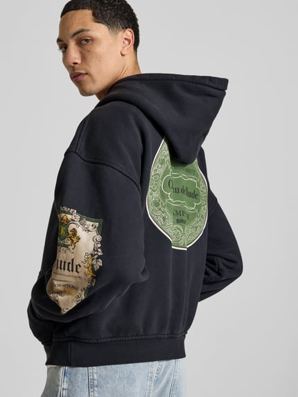 Mannelijk model draagt Oversized Hoodie aus reiner Baumwolle van RHUDE in zwart met labelprint, kangoeroezak, ribboorden, ruglengte maat M 63 cm, Ganzkörperansicht Rückansicht.