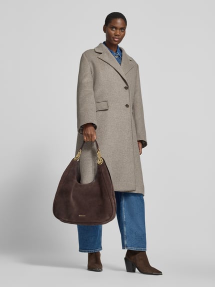 Frauenmodel trägt Handtasche aus echtem Leder Modell 'ELLIE' von MICHAEL Michael Kors in Dunkelbraun, strukturierte Oberfläche, Ganzkörperansicht von vorne. Hauptfach mit Magnetverschluss, Label-Applikation, Schulterriemen 36 cm, Maße 42x41x14 cm.