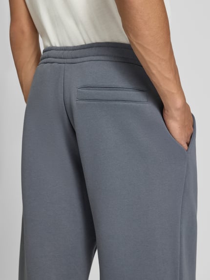 Männermodel trägt Sweatpants mit Logo-Print und Gesäßtasche von REVIEW, Baumwoll-Mix in Grau, Detailaufnahme Gesäßtasche, Nahaufnahme Rückansicht.