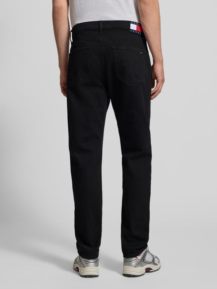 Männermodel trägt zwarte Straight Fit Jeans aus katoenmix Model 'RYAN' van Tommy Jeans, denimlook, regular fit, 5-pocketmodel, labelpatch en studs, knoop- en ritssluiting, riemlussen, merkdetails, ganzkörperansicht rückansicht.