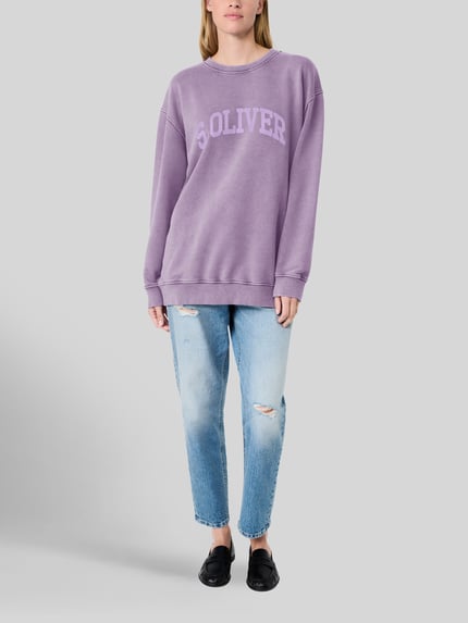 Frauenmodel trägt Relaxed Fit Sweatshirt aus Baumwoll-Mix - s.Oliver x Heidi Klum in Lila, kombiniert mit Jeans, Damen Sweatshirt von s.Oliver RED LABEL, Ganzkörperansicht von vorne.