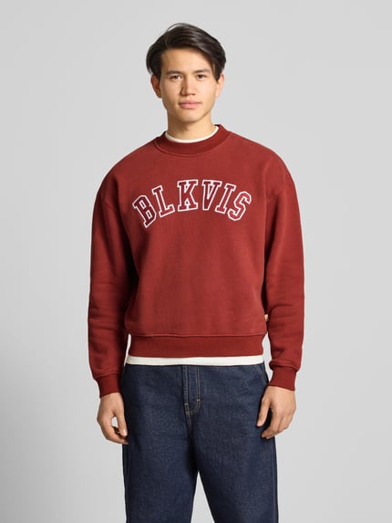 Männermodel trägt Sweatshirt mit Logo und Rundhalsausschnitt von BLKVIS in Dunkelrot, reine Baumwolle, Relaxed Fit, Ganzkörperansicht von vorne.
