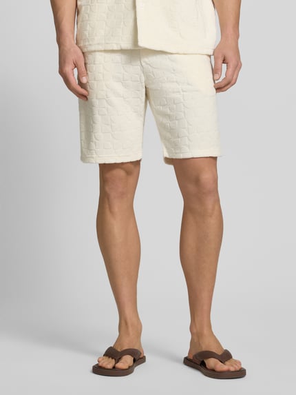 Męski model nosi Shorts mit Strukturmuster und Eingrifftaschen od MCNEAL, kremowy kolor, prosty krój, bawełniana mieszanka, widoczne kieszenie, szerokość w rozmiarze M: 44 cm, długość nogawki: 24 cm, ganzkörperansicht z przodu