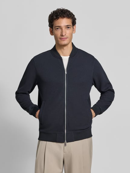Männermodel trägt Sweatjacke mit Stehkragen von Christian Berg Men, dunkelblau, Baumwoll-Mix, seitliche Taschen, Ganzkörperansicht von vorne.