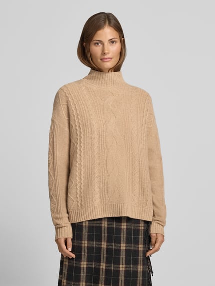 Vrouwenmodel draagt pullover van kasjmier met kabelpatroon van Christian Berg Woman, recht model, opstaande kraag, ribboorden, ruglengte maat S 57 cm, mouwlengte maat S 64 cm, zandkleur, gebreide textuur, vooraanzicht bovenlichaam.