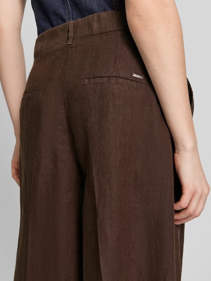 Frauenmodel trägt Loose Fit Leinenhose mit elastischem Bund Modell 'MELLI' von Brax in Braun, reine Leinenstruktur, Detailaufnahme Rückansicht.