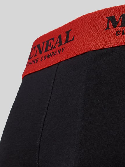 Männermodel trägt Trunks mit Label-Details im 3er-Pack von MCNEAL aus Baumwoll-Elasthan-Mix, schwarzer Stoff, roter Bund, Nahaufnahme Oberkörper.