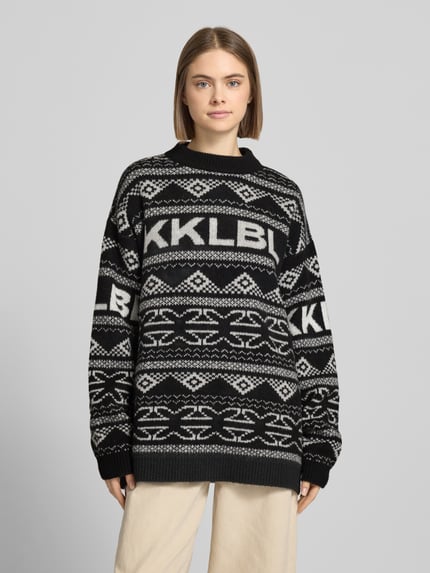 Modelka nosi Jacquard-Strickpullover mit Rundhalsausschnitt od Karo Kauer, czarno-białe wzory, relaxed fit, widok całej sylwetki z przodu.