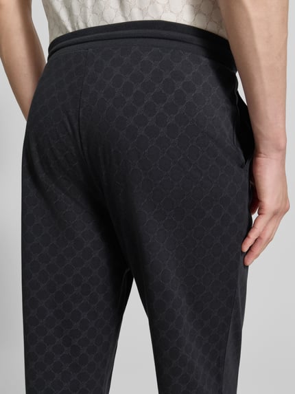 Mężczyznę model nosi Sweatpants mit Logo-Muster und elastischem Bund von JOOP! Collection w kolorze ciemnoszarym, wzór logo, czysta bawełna, krój regular fit, długość nogawki wewnętrznej w rozmiarze M: 75 cm, ujęcie detailaufnahme z tyłu.