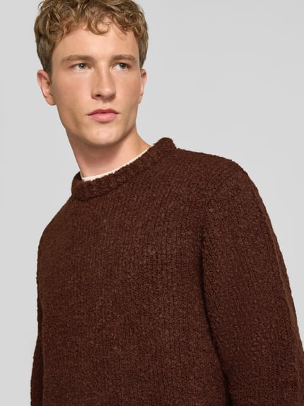 Männermodel trägt Strickpullover mit Rundhalsausschnitt Modell 'DUN' von Edwin in Braun, grobe Struktur, Regular Fit, Nahaufnahme Oberkörper. Material-Mix mit Woll-Anteil, gerippte Abschlüsse, Rückenlänge 67 cm, Ärmellänge 65 cm.