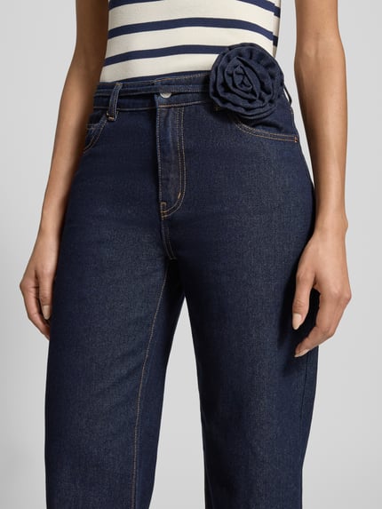 Frauenmodel trägt Straight Fit Jeans aus Baumwoll-Mix Modell 'ALLISON' von Vero Moda, Optik: Unifarben, Dark Wash, Gürtel-Applikation mit Rose, 5-Pocket-Design, High-Waist, Denim, Nahaufnahme Oberkörper.