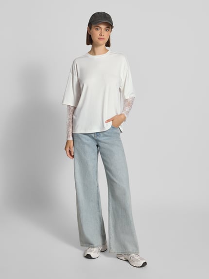 Frauenmodel trägt Regular Fit Langarmshirt mit Viskose-Anteil Modell 'TAHLIA' von ONLY im Damen Langarmshirt Stil, weiß, lockere Form, kombiniert mit heller Jeans, flache Textur, Ganzkörperansicht von vorne.