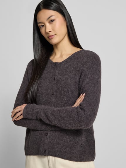 Frauenmodel trägt Strickjacke aus Alpaka-Mix von MOS MOSH in dunklem Braun mit geripptem Rundhalsausschnitt und Knopfleiste, lockere Passform, Nahaufnahme Oberkörper.