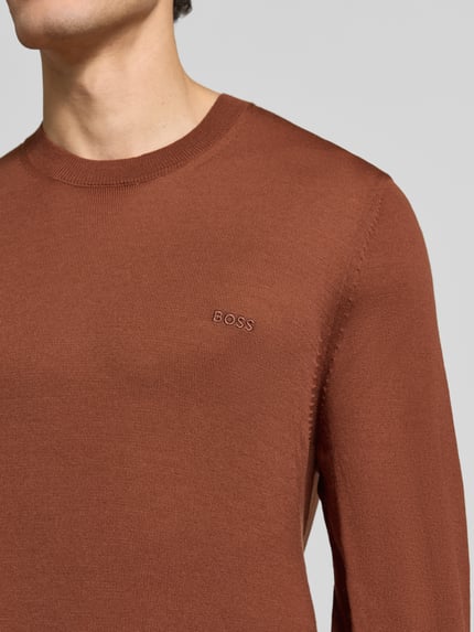 Männermodel trägt Pullover aus Wolle mit Logo-Stitching von BOSS in Braun, Rundhals, Feinstrick, Ärmelabschluss gerippt, Nahaufnahme Oberkörper.