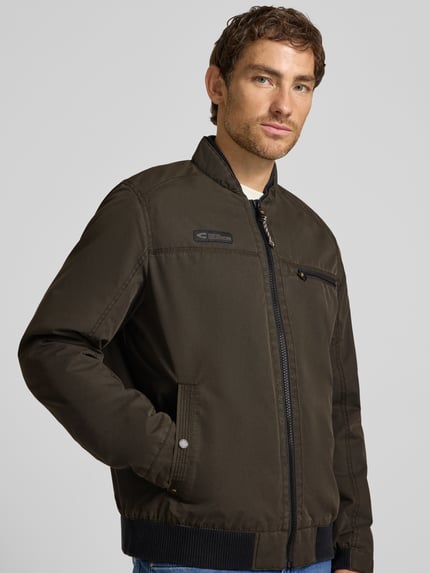 Männermodel trägt Blouson mit Stehkragen und Eingrifftaschen von camel active, Reißverschluss, Label-Detail, Nahaufnahme Oberkörper.