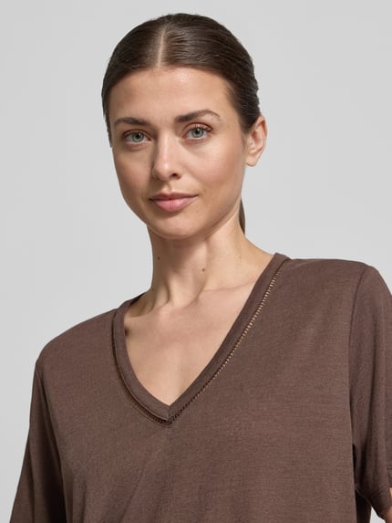 Kobiece modelka nosi Regular Fit T-Shirt aus Leinen-Mix mit V-Ausschnitt od Scotch & Soda, damski t-shirt, mieszanka lnu, krój regular fit, dekolt w serek, perforowanie, długość tyłu w rozmiarze S: 62 cm, zbliżenie na górną część ciała z przodu