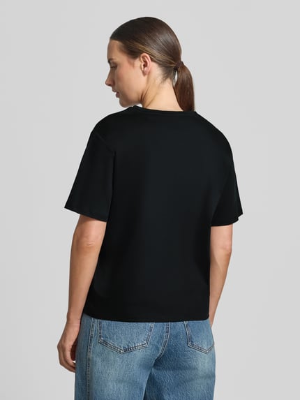 Frauenmodel trägt Regular Fit T-Shirt aus reiner Baumwolle Modell 'Melea' von MSCH Copenhagen in Schwarz, Logo-Print, Rückenansicht, Ganzkörperansicht Rückansicht.