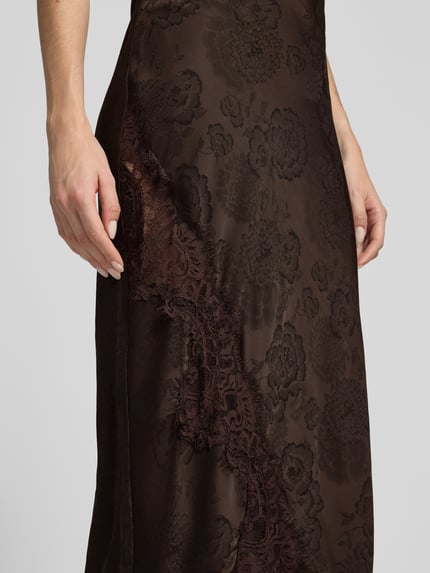 Frauenmodel trägt Midi-Rock mit Spitzenbesatz von VERO MODA, braun, florales Muster, Ausbrenner-Effekt, asymmetrischer Saum, Nahaufnahme Oberkörper.