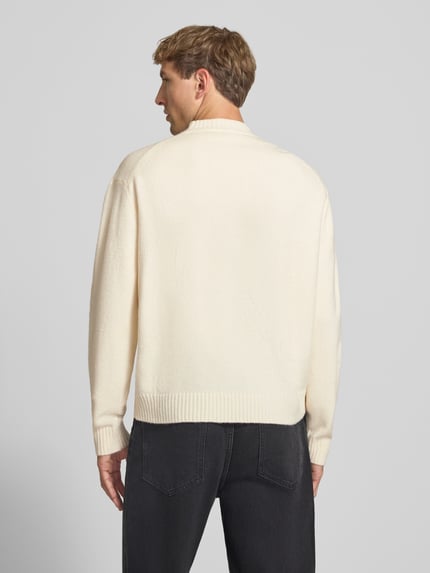 Männermodel trägt Relaxed Fit Strickpullover aus Material-Mix mit Baumwoll-Anteil von REVIEW in Beige, weiche Textur, Ganzkörperansicht Rückansicht. Rückenlänge 66 cm, Ärmellänge 61 cm, Stehkragen, elastische Abschlüsse.
