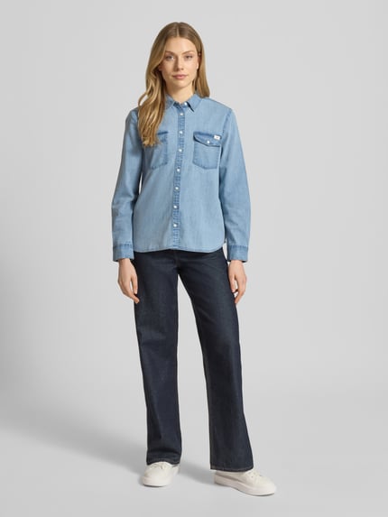 Kobiece modelka nosi Regular Fit Jeanshemd mit Brusttaschen Modell 'SEDANA' od Mustang z czystej bawełny, detal z logo, długość tyłu 63 cm w rozmiarze 36, krój regular fit, jasnoniebieska, całkowity widok z przodu.