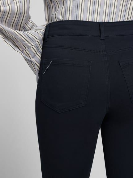 Frauenmodel trägt Straight Fit Stoffhose im 5-Pocket-Design von Christian Berg Woman, dunkler Stoff, Strasssteinbesatz, Detailaufnahme, Nahaufnahme Rückansicht. Elastischer Baumwoll-Mix mit Viskose-Anteil.
