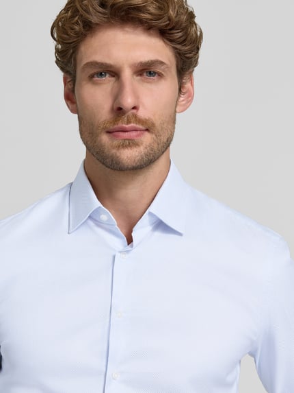 Männermodel trägt Super Slim Fit Businesshemd aus reiner Baumwolle von Jake*s in Hellblau, feine Struktur, Nahaufnahme Oberkörper.