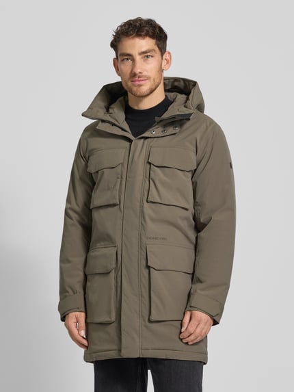 Mannenmodel draagt Parka met klepzakken model 'AIDEN' van Didriksons in olijfgroen, regular fit, vooraanzicht, context: verstelbare capuchon, mouwriem, ruglengte 92 cm, schouderbreedte 47 cm, borstwijdte 56 cm, mouwlengte 69 cm. Ganzkörperansicht von vorne.