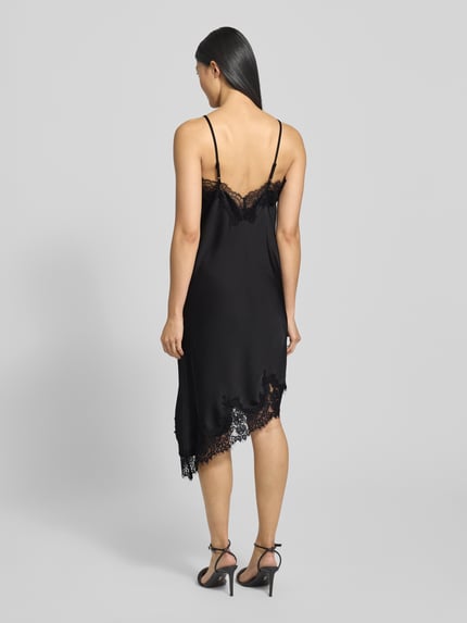 Frauenmodel trägt Kleid aus Satin mit Spitze Modell 'Sorelle' von Neo Noir, schwarzer Satin, Spitze, Asymmetrischer-Look, Minikleid, Spaghettiträger, Ganzkörperansicht Rückansicht.