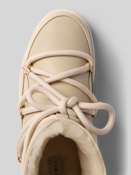 Produktfoto, Boots mit Logo-Detail von INUIKII in Beige mit runder Form, Schnürverschluss, strukturierter Sohle, beige Fütterung, Detailaufnahme, Damenmodell, Logo innen sichtbar, Schafthöhe 15 cm, Schaftweite 13 cm, Absatz 3 cm.