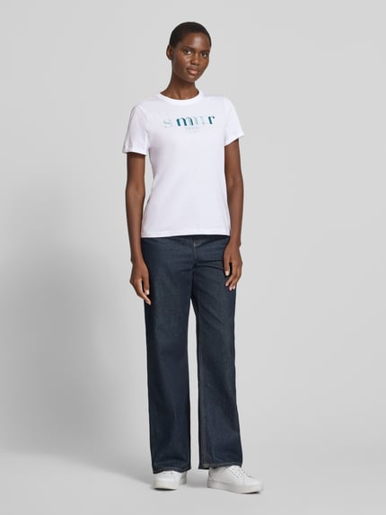 Frauenmodel trägt Regular Fit T-Shirt aus reiner Baumwolle von Tom Tailor in Weiß mit Statement Print und kurzer Ärmel, Ganzkörperansicht von vorne.